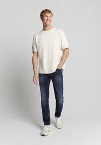 Crème short-sleeve t-shirt met een ronde hals, gecombineerd met donkerblauwe spijkerbroeken en lichtgekleurde sneakers. Glad materiaal, relaxte pasvorm.