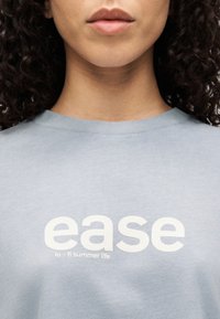 Svetlomodra jopa z rebrastim ovratnikom in velikim belim napisom "ease" ter manjšim napisom pod njim, ki pravi "lo-fi summer life."