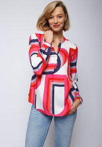 Farbiger Langarmshirt mit kräftigen geometrischen Mustern in Rot, Pink und Marineblau auf einem weißen Hintergrund. Leichter Stoff, lockere Passform.