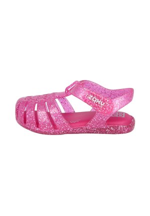 Sandalias brillantes rosas con un diseño abierto, que presentan cortes laterales y una correa ajustable. Hechas de un material plástico flexible.