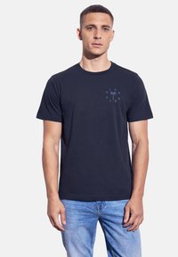 Mörkblå bomull t-shirt med kort ärm, prydd med en palmbild och texten "HIGH TIDE" i ljusblått på bröstet.