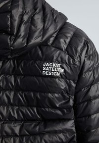 Veste noire isolante avec un motif matelassé et une capuche. Comprend un texte blanc "JACK1T SATELITE DES1GN" sur le tissu. Texture brillante et lisse.