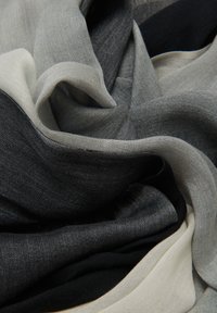 Écharpe légère et superposée présentant un dégradé de couleurs noir, gris et blanc cassé ; tissu doux et fluide avec une texture lisse.