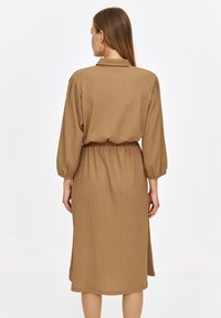 Brązowa, teksturowana sukienka koszulowa z kołnierzykiem, długimi puff sleeves i elastycznym paskiem w talii. Długość do połowy łydki, w luźnym kroju.