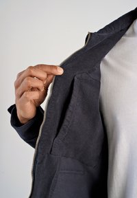 Granatowa kurtka zapinana na zamek, o miękkiej fakturze, z widoczną kieszenią po lewej stronie oraz srebrnym zamkiem błyskawicznym na tle jasnoszarego t-shirta.