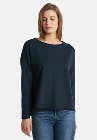 Navy sweatshirt with a smooth texture, wide neckline, and long sleeves, paired with light blue denim jeans.