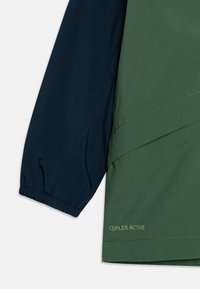 Manche de veste verte et marine avec poignet élastique. Présente une finition texturée et l'impression "CEPLEX ACTIVE" en vert clair sur l'ourlet.