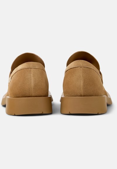 Par af tanfarvede ruskindsløbehjul med tykke gummisåler vist bagfra på en ensartet lys baggrund.