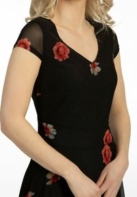 Vestido negro con mangas cortas transparentes, escote en V y patrones florales en rojo y azul. Textura suave con un torso ajustado y falda acampanada.