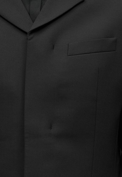 Veste de costume noire avec revers cranté et poche poitrine passepoilée, boutonnière cousue sur le côté gauche.