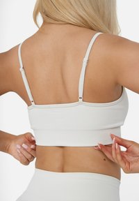 Hellgraues, geripptes Crop Top mit dünnen, verstellbaren Trägern und figurbetonter Passform, das eine glatte Textur und subtile Nähte zeigt.
