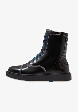 Botte haute en cuir noire avec lacets bleus, coutures blanches, semelle noire épaisse et écusson logo cousu au talon.