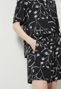 Svart topp och shorts-set med blommönster i vitt. Toppen har korta ärmar och V-ringning, med en avslappnad passform och sidofickor.