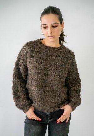 Bruine gebreide trui met een textuurpatroon, ronde halslijn en verlaagde schouders, gecombineerd met donkere spijkerbroeken.