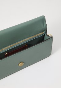 Rectangular green leather wallet with a gold zipper, a golden logo accent, and interior card slots visible. Textured finish.
