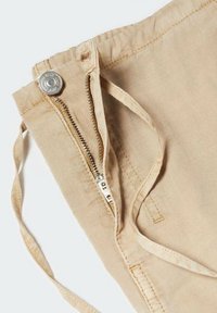 Shorts en lin beige avec une fermeture éclair à l'avant et un bouton en métal, dotés de liens à la taille et d'une finition lisse et texturée.