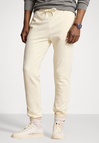 Krämfärgade sweatpants i mjukt tyg med elastisk midja och justerbar dragsko. Bärs med vita sneakers och ljusa strumpor.