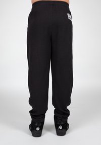 Sorte joggers med vaffelstrik, der har en elastisk talje. Bagpå er der et hvidt mærke, og de er parret med sorte sneakers prydet med et gorilla-graphic.