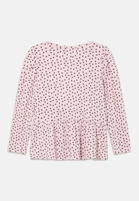 Ροζ τοπ με μακριά μανίκια και βολάν στο τελείωμα, διακοσμημένο με μαύρα πουά και ριμπ υφή. Στρογγυλή λαιμόκοψη στο πίσω μέρος.