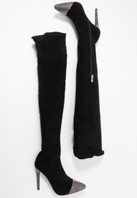 Mustat polven yli ulottuvat saappaat, jotka on valmistettu pehmeästä sametista; korkea stiletto-korko, hopeiset strassikoristeet kärjessä, vetoketjuyksityiskohta sivussa.