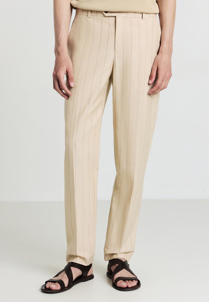 Beige gestreifte Hose aus leichtem Stoff, mit taillierter Passform, geraden Beinen und Seitentaschen, kombiniert mit dunkelbraunen Sandalen.