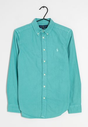 Camicia turchese a maniche lunghe con bottoni, colletto e logo ricamato bianco, appesa a una gruccia nera su sfondo bianco.