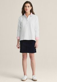 Vit långärmad skjorta med en rosa krage, i kombination med en mörk marinblå kjol. Bärs med vita sneakers och en enkel design.