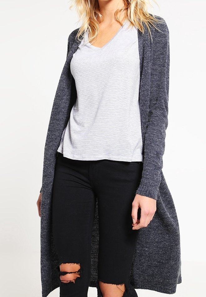 Lång grå cardigan i texturerad stickad tyg, bärs över en randig t-shirt med v-ringning, matchad med svarta slitna jeans.