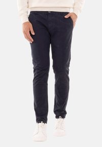 Chinos blu navy in cotone, slim fit con tasche, abbinati a sneakers bianche. Texture liscia, minimo dettaglio di cucitura.
