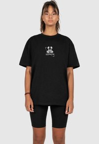 Sort bomulds t-shirt med løs pasform, korte ærmer og et grafisk print med to figurer og tekst på brystet, parret med sorte cykeltights.