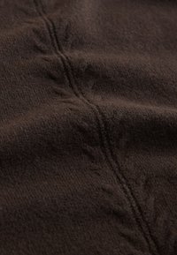 Dark brown textured fabric with visible soft fibers and a subtle seam running vertically, featuring a slight leaf pattern along the edge.