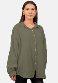 Overmaatse olijfgroene knoopshirt gemaakt van textuurstof met een kraag en lange mouwen, voorzien van vijf knopen aan de voorkant.