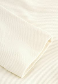 Ribbed cream-colored fabric with a smooth texture. The image focuses on a folded sleeve displaying neat stitching and seam detail.