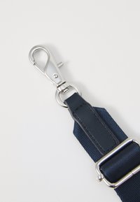 Navytygrem strap med en silverfärgad metallklämma och beslag. Strukturerad yta med en slät läderdetalj vid fästpunkten.
