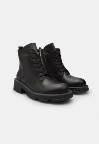Botines de cuero negro con cierre de cordones en la parte delantera, cremallera lateral, paneles texturizados y suela gruesa. Presentan una punta redondeada y un diseño resistente.