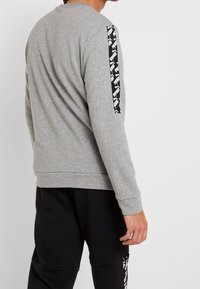 Szary sweatshirt z długimi rękawami, z czarnym wzorem na lewym ramieniu. Prosty design i miękka tekstura.