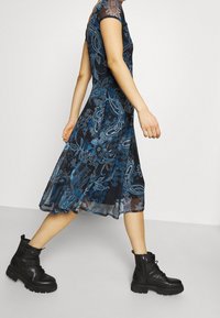 Vestido negro con estampado de cachemira azul, mangas cortas y falda fluida, combinado con botas de combate negras de suela gruesa.