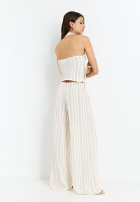 Completo a righe in due pezzi: top bandeau corto e pantaloni a gamba larga in tessuto leggero. I colori sono crema con sottili strisce scure; finitura textured.