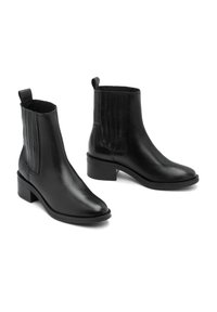 Une paire de bottines en cuir noir avec de petits talons carrés et des panneaux latéraux élastiques, présentées sur un fond blanc.
