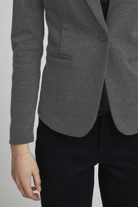 Blazer gris con un acabado texturizado, cierre de un solo botón y dos bolsillos frontales, combinado con pantalones oscuros.