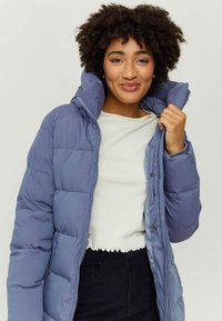 Puffer jacket in light blue nylon with a high collar, featuring quilted texture, front zipper, and side pockets. Worn over a white top.