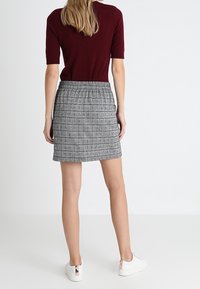Minifalda a cuadros grises con cintura elástica, combinada con una blusa de manga corta en burdeos. Zapatillas blancas con un acento en oro rosa.
