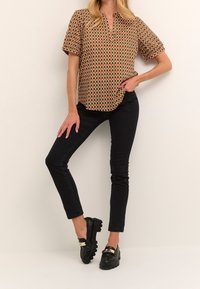 Blouse à manches courtes avec col, ornée d'un motif losange multicolore aux tons terreux. Portée avec un pantalon noir slim et des mocassins noirs.