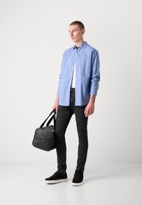 Camisa de botón azul claro, jeans negros, zapatillas negras y un bolso negro. La camisa tiene un bolsillo en el pecho y un logo sutil.