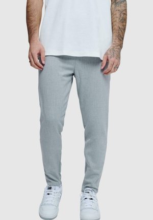 Pantalones tapered en gris claro, hechos de una tela texturizada, combinados con zapatillas blancas. Presentan un corte ajustado y una cinturilla elástica para mayor comodidad.