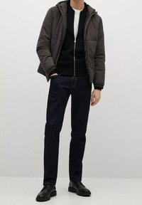 Dunkelgraue Herrenjacke mit Reißverschluss und Kapuze, schwarzer Pullover mit Reißverschluss und dunkelblaue Jeans. Schwarze Lederschuhe vervollständigen den Look.