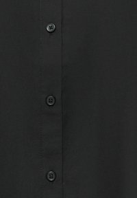 Gros plan d’un tissu noir avec une rangée verticale de quatre boutons noirs assortis cousus à travers quatre trous chacun.