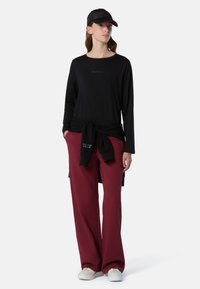 Maglietta nera a maniche lunghe con logo 'NORTH SAILS'; pantaloni bordeaux a vestibilità ampia; cappellino nero; sneaker bianche; look rilassato e casual.
