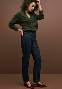 Zelený pletený cardigan s výstřihem do V a dvěma knoflíky, kombinovaný s tmavomodrými džínami s vysokým pasem a bordó podpatkovými mule.