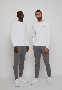 White sweatshirts with yellow logo accents, paired with gray joggers and white sneakers. Simple, casual design and comfortable fit.